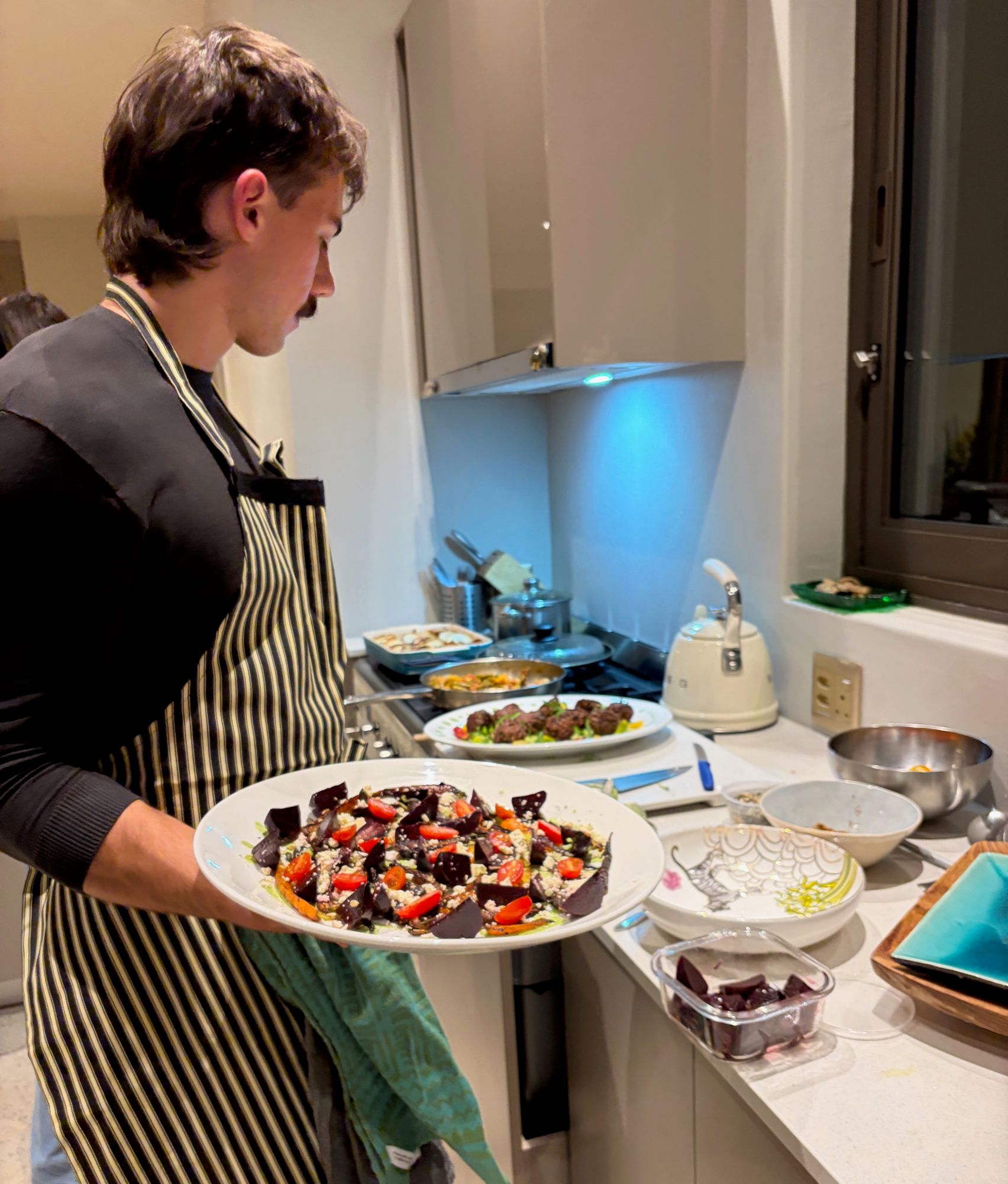 Matthew carrying a beetroot salad through a villa kitchen, with more dishes ready on the counter