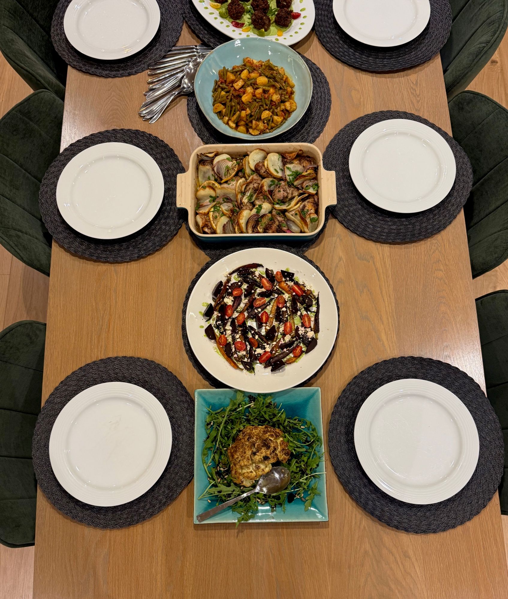 A table laid for six with a beetroot and feta salad, a potato and onion bake, green beans, meatballs and roast cauliflower on rocket
