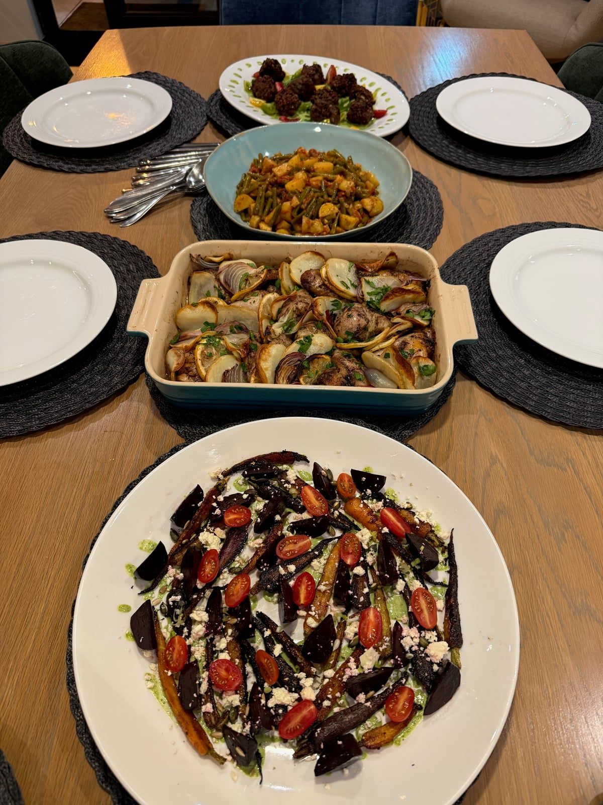 A table laid for six with roast beetroot and carrots with feta and cherry tomatoes, chicken baked with potatoes and red onion, green beans with potatoes, and meatballs